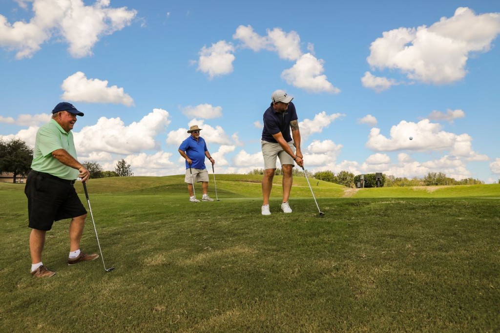 Three golfers on a sunny fairway, one mid-swing